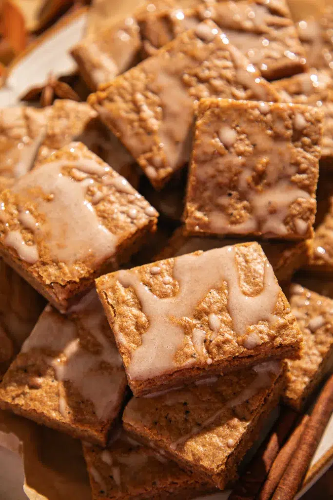 Overhead shot of gingerbread bars on a plate lined with parchment, drizzled with espresso glaze, styled with ribbons and a mug of coffee for a warm holiday setting.