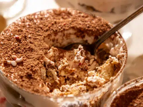Side view of a tiramisu cup with a spoon showing layers of espresso-soaked ladyfingers and peppermint mascarpone cream.