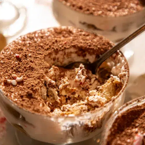Side view of a tiramisu cup with a spoon showing layers of espresso-soaked ladyfingers and peppermint mascarpone cream.