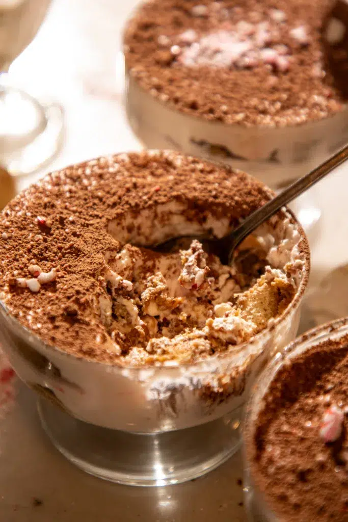 Side view of a tiramisu cup with a spoon showing layers of espresso-soaked ladyfingers and peppermint mascarpone cream.