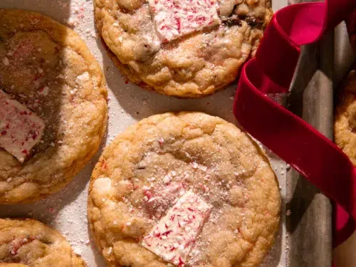 Fresh baked peppermint bark pretzel cookies on a parchment lined baking tray with a red velvet ribbon for a festive touch.