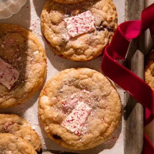 Fresh baked peppermint bark pretzel cookies on a parchment lined baking tray with a red velvet ribbon for a festive touch.