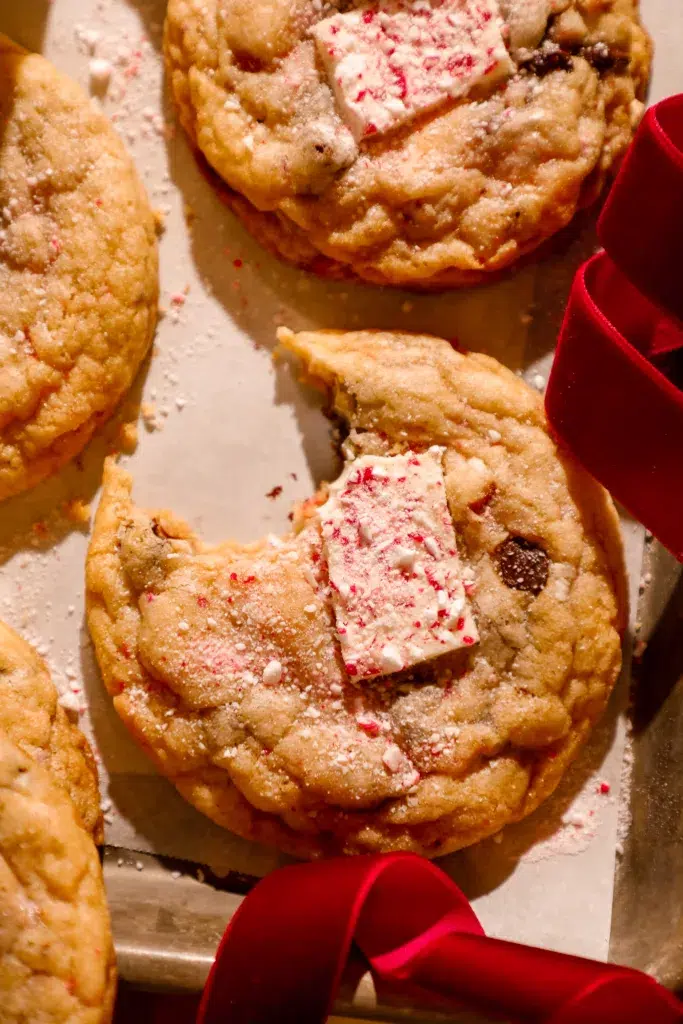 Chewy peppermint bark pretzel cookie with a piece of peppermint bark on top and a bite taken out.