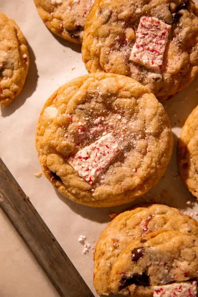 Several golden peppermint bark pretzel cookies on parchment paper, each with chocolate pieces and peppermint bark mixed in.