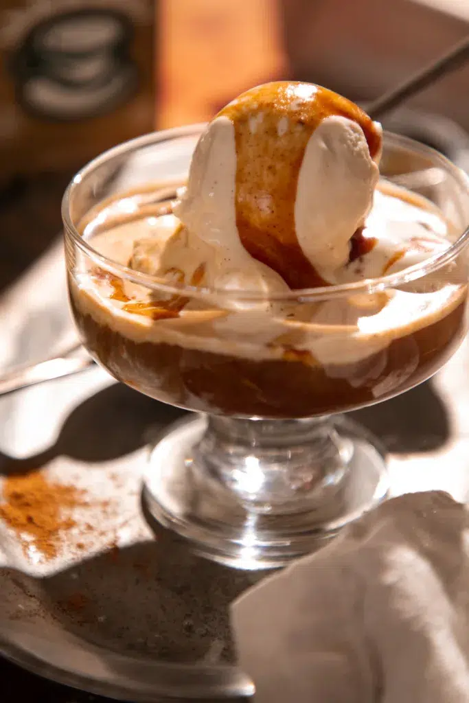 Overhead view of eggnog affogato topped with caramel beside a carton of AE Dairy eggnog and a small cup of espresso.