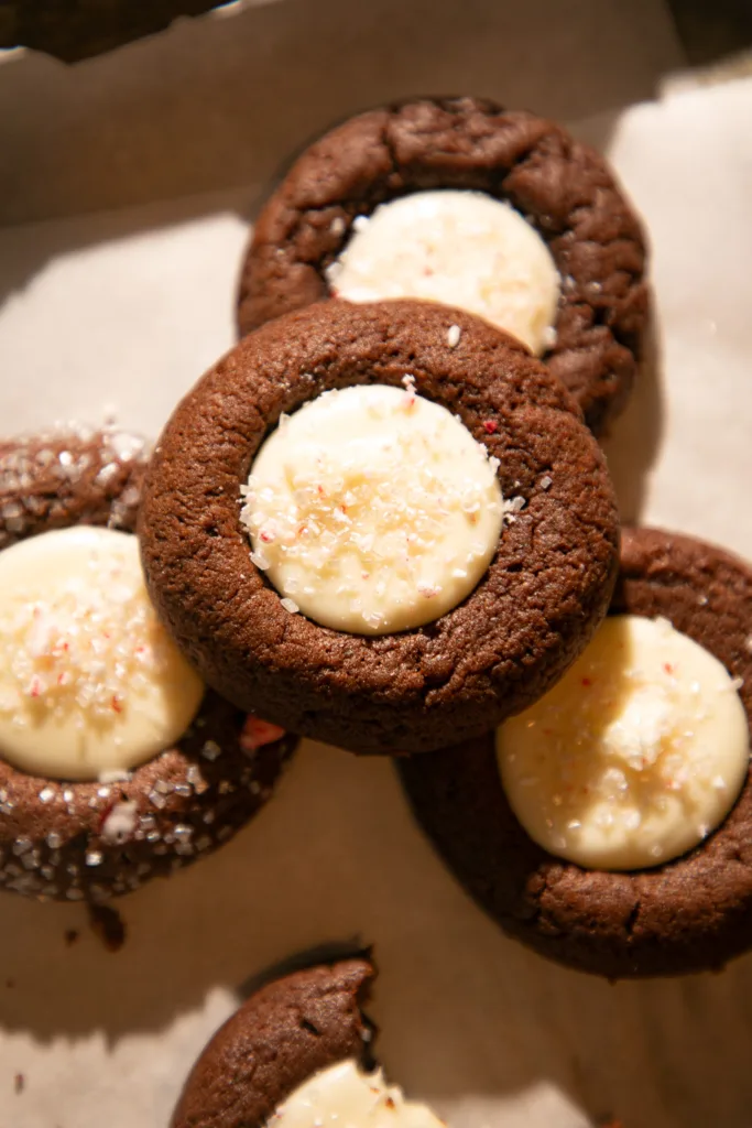 Several chocolate peppermint thumbprint cookies with creamy white centers stacked on a baking tray.