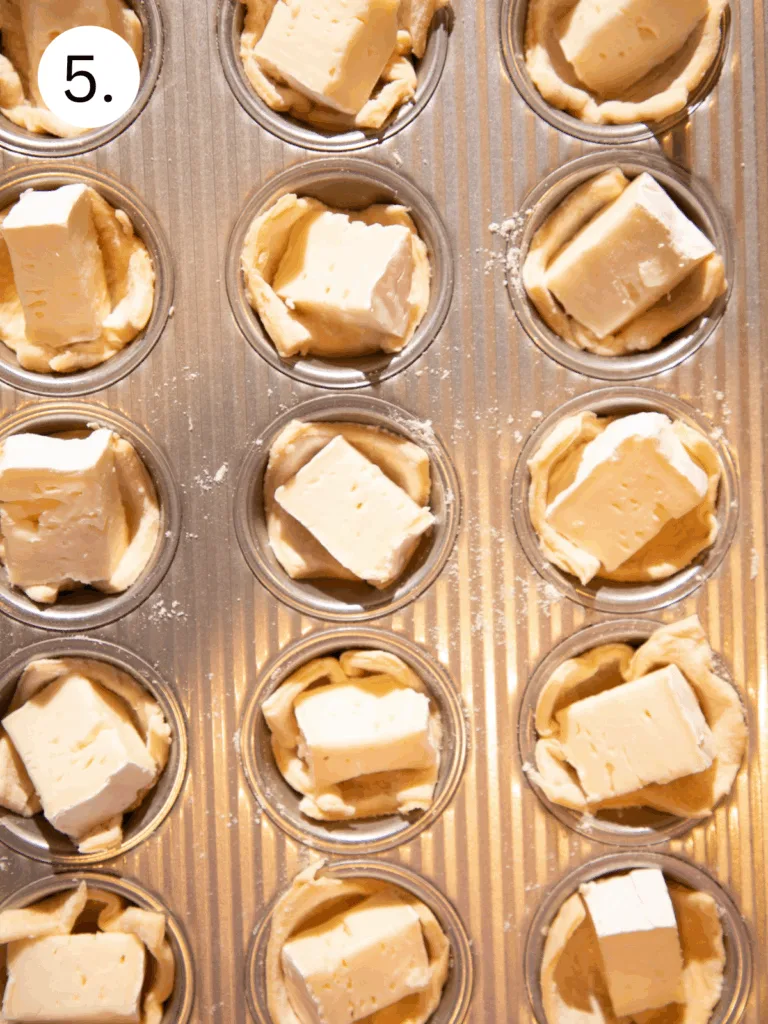 Crescent dough cups filled with cubes of brie cheese before baking.