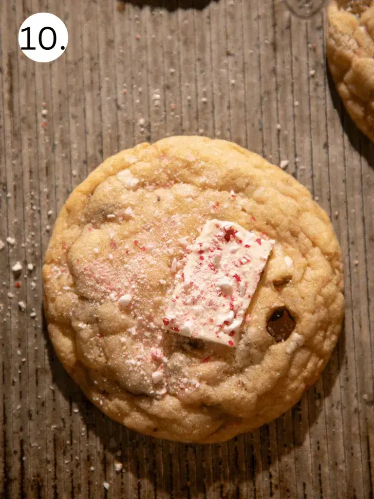 Soft and chewy peppermint bark pretzel cookie topped with a piece of crushed peppermint bark on a baking sheet.