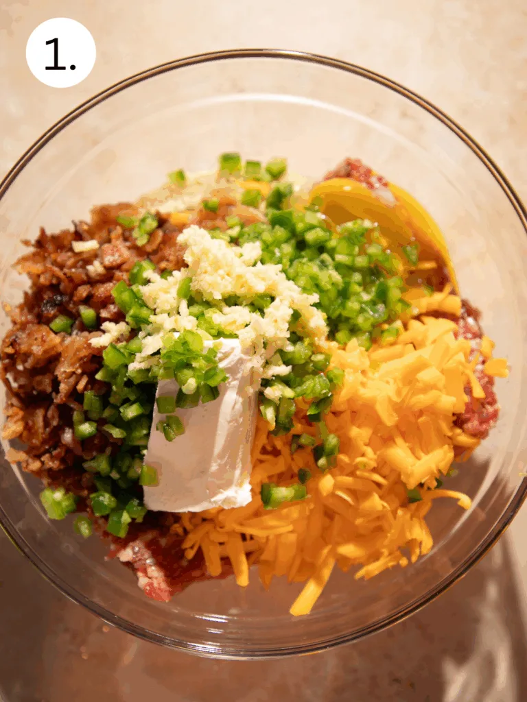 Mixing bowl with sausage, jalapeños, garlic, bacon, cream cheese, and cheddar before combining.
