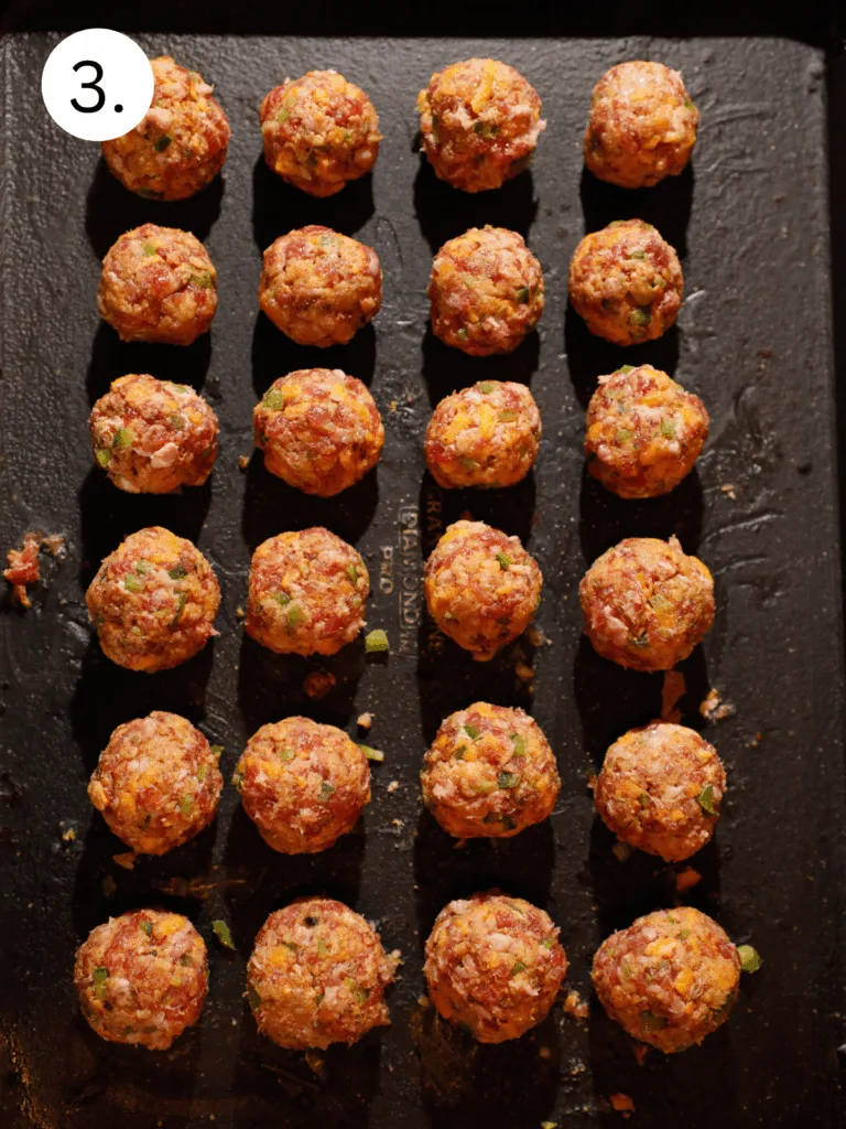 Raw jalapeño popper meatballs arranged in rows on a baking sheet before baking.
