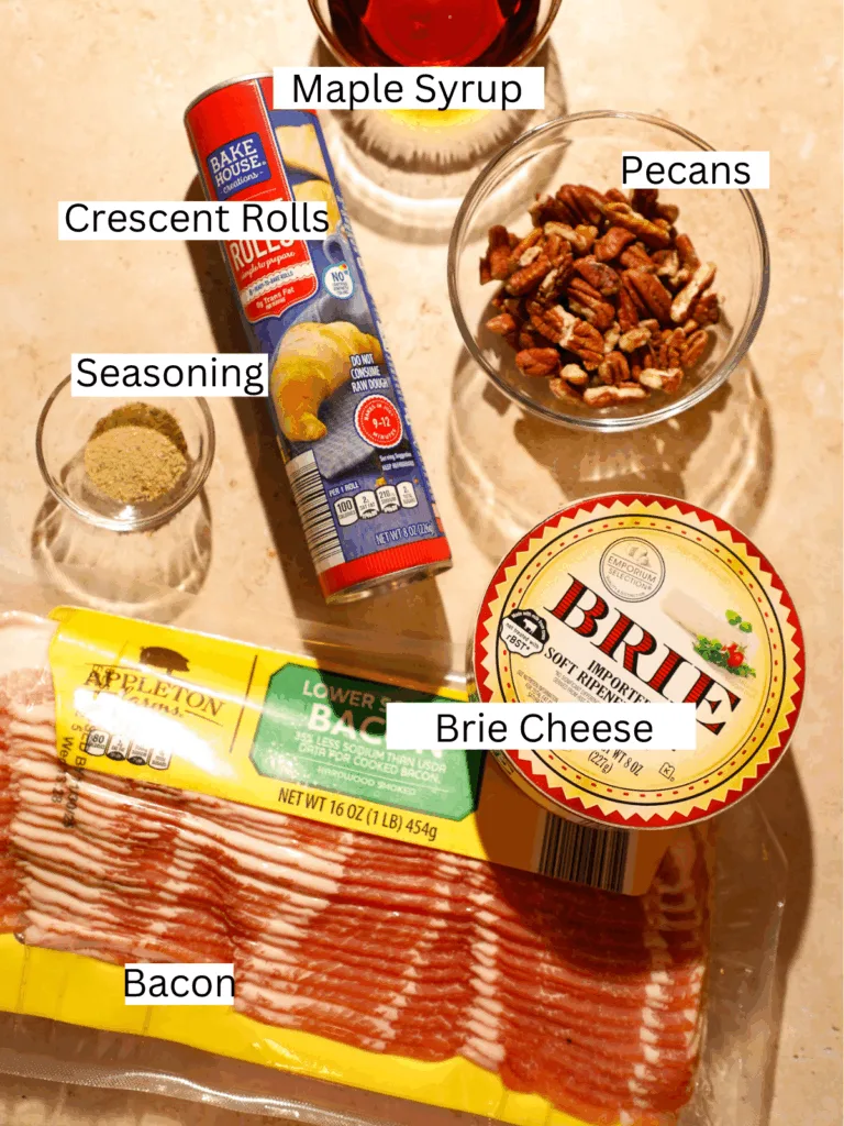 Ingredients for maple bacon brie crescent bites including bacon, brie, maple syrup, crescent dough, pecans, and seasoning.
