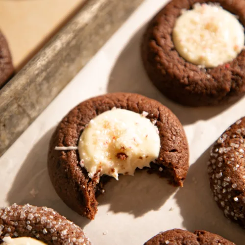 Close-up of chocolate peppermint thumbprint cookie with creamy white chocolate center and a bite taken out.