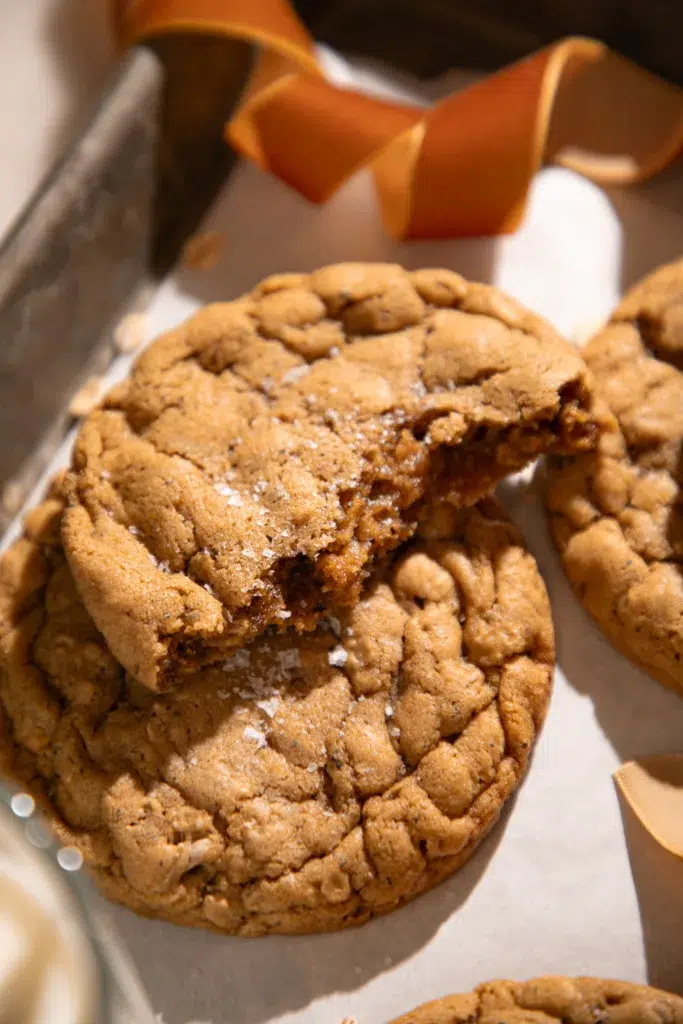 Close-up of a broken gingerbread oatmeal cookie showing a soft interior with molasses and spices. Flaky sea salt is visible on top.