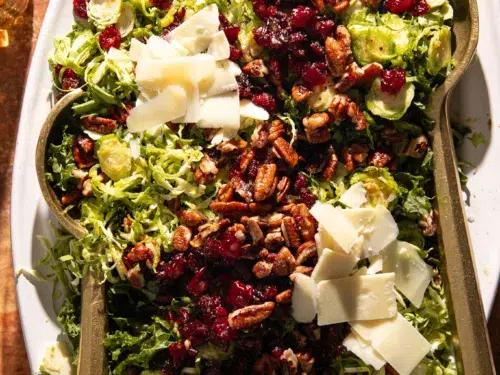 Bright and colorful Brussels sprout and kale salad with maple dressing, dried cranberries, toasted pecans, and shaved cheese arranged on a serving platter.