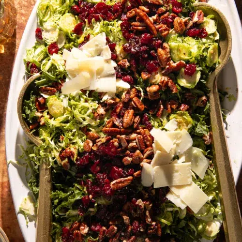 Bright and colorful Brussels sprout and kale salad with maple dressing, dried cranberries, toasted pecans, and shaved cheese arranged on a serving platter.