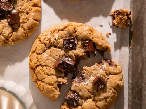 Close up of a brown butter espresso oatmeal chocolate chunk cookie with melty chocolate pools and flaky sea salt on top.