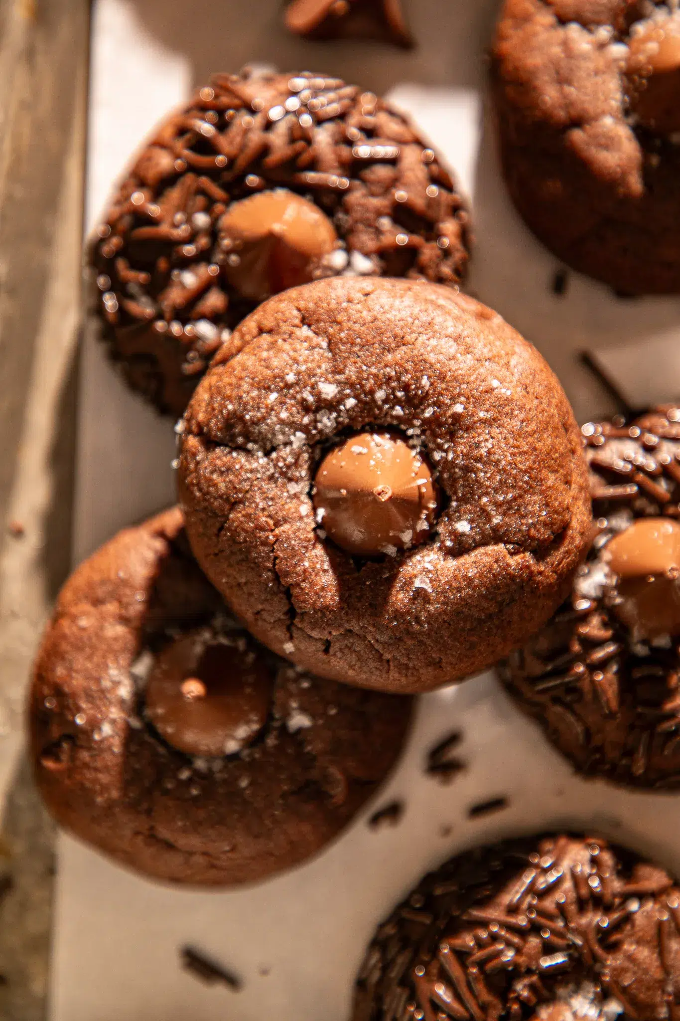 Close-up chocolate espresso blossom cookie topped with a chocolate kiss and flaky sea salt over parchment.