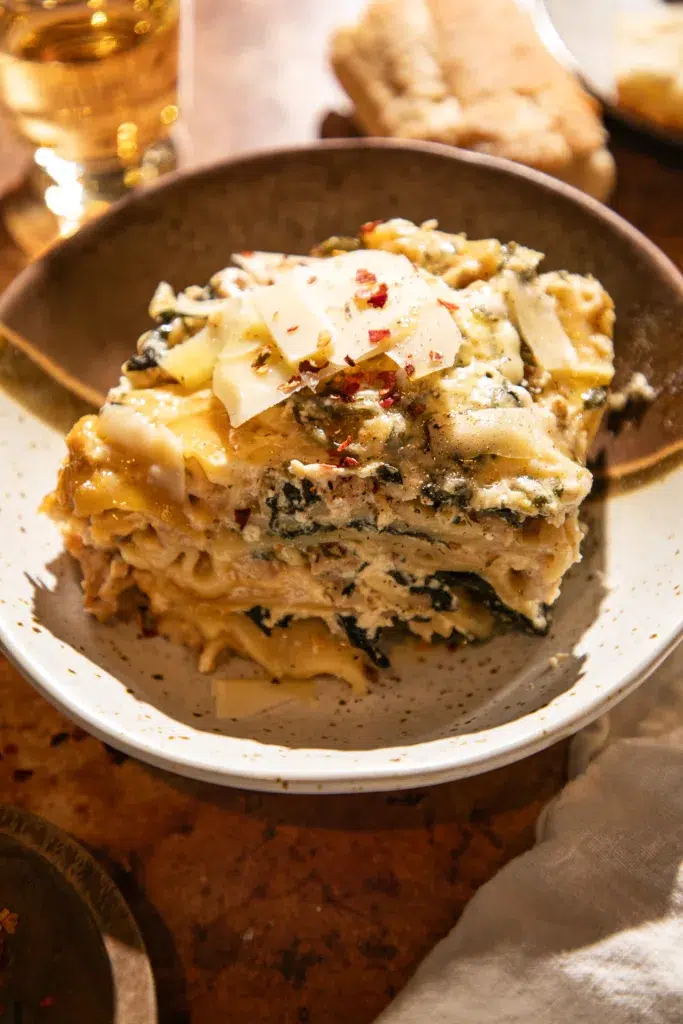 Slice of slow cooker white chicken lasagna served in a bowl with melted cheese and spinach.