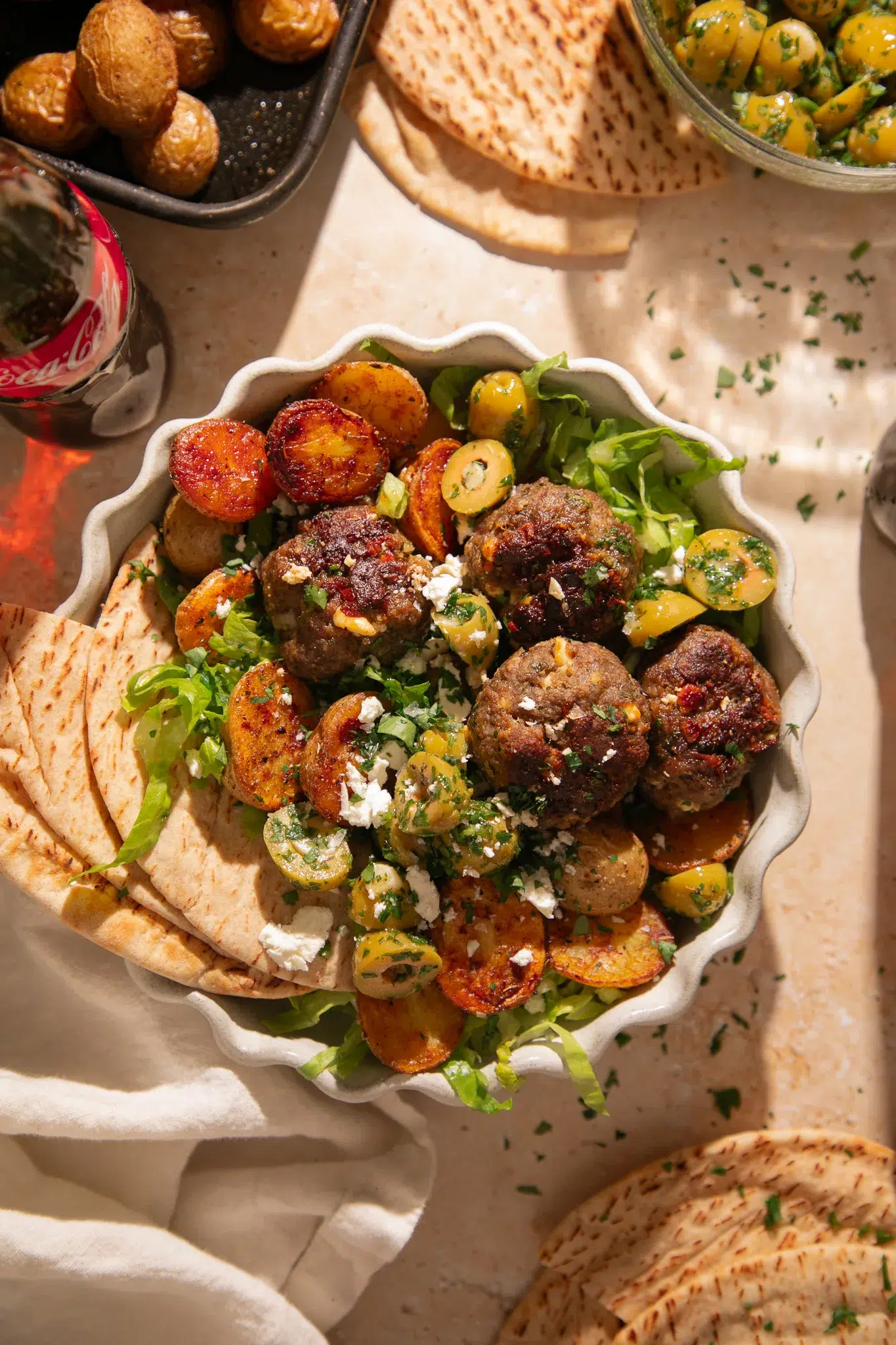 Close up of lemon feta meatballs with a golden crust, roasted baby potatoes, chopped herbs, and crumbled feta cheese.