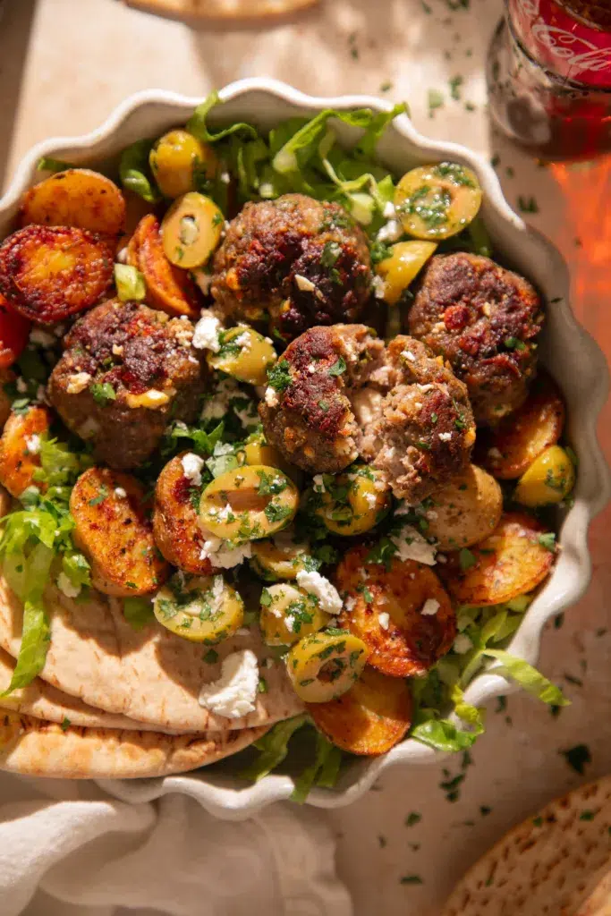 The Hearty Life Everyday Blend seasoning jar styled next to sheet pan lemon feta meatballs and roasted potatoes.