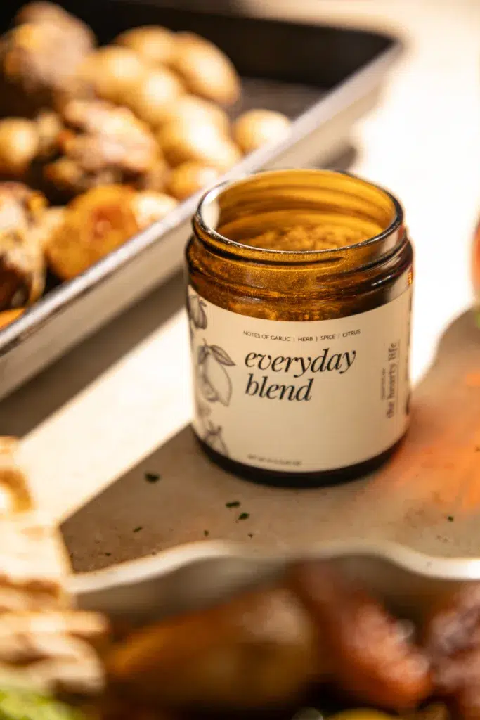 The Hearty Life Everyday Blend seasoning jar styled next to sheet pan lemon feta meatballs and roasted potatoes.