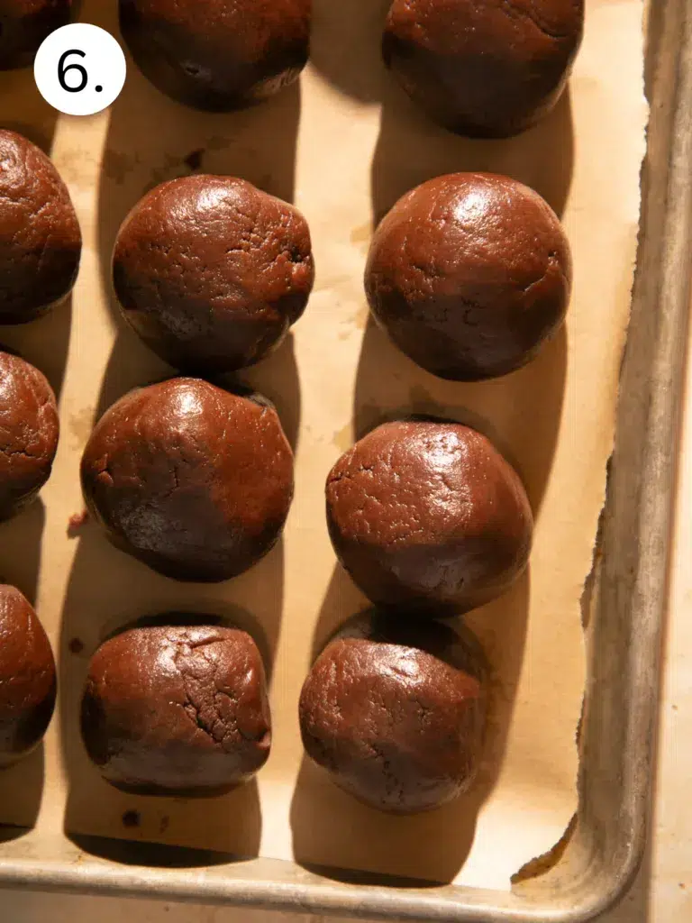 Scoops of double chocolate espresso cookie dough on a parchment lined baking sheet before rolling into balls.