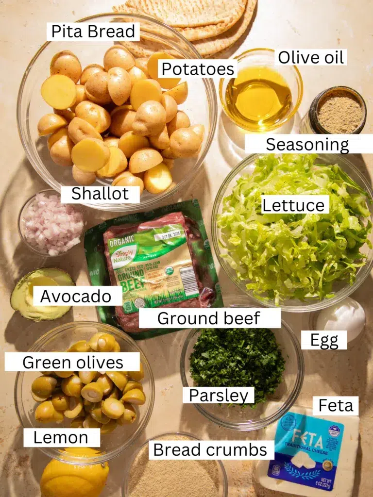 Ingredients for sheet pan lemon feta meatballs with roasted potatoes, including ground beef, feta cheese, baby potatoes, green olives, lemon, parsley, pita bread, olive oil, and seasoning.