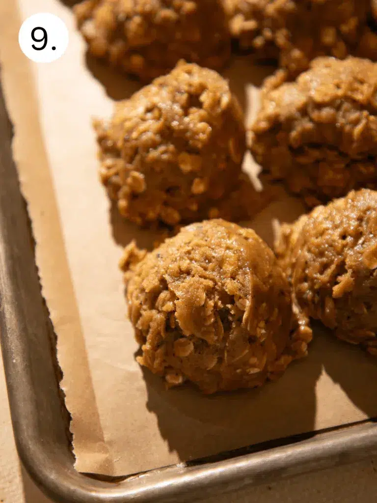 Scoops of gingerbread oatmeal cookie dough on a parchment-lined baking sheet, ready to chill or bake. The dough is thick, speckled with oats, and lightly glossy with molasses.