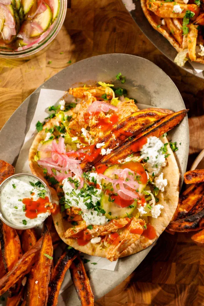 Sheet pan buffalo chicken pita dinner with sweet potato fries, yogurt dipping sauce, and fresh herbs on a serving platter.