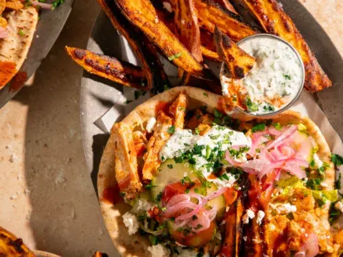 Close-up of buffalo chicken pitas topped with creamy yogurt sauce, pickled red onions, sliced cucumbers, and crumbled feta.
