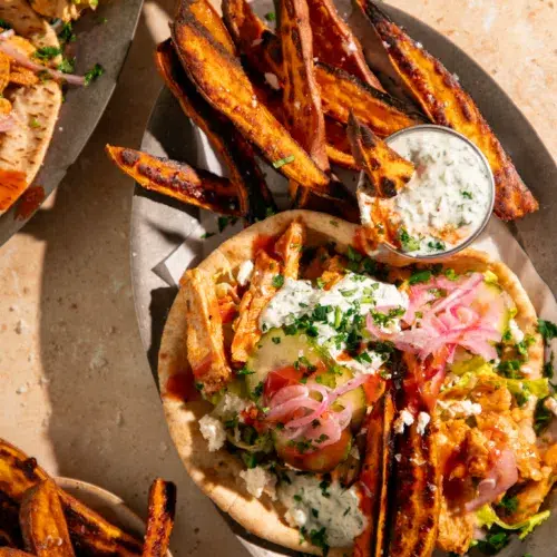 Close-up of buffalo chicken pitas topped with creamy yogurt sauce, pickled red onions, sliced cucumbers, and crumbled feta.