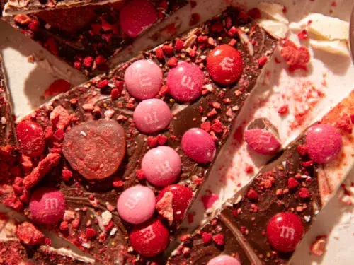 Overhead view of sliced no-bake Valentine’s Day gummy bark on parchment paper with heart gummies, M&Ms, and crushed strawberry pieces.