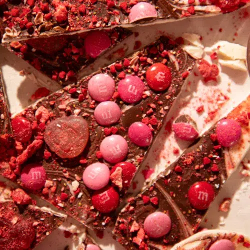 Overhead view of sliced no-bake Valentine’s Day gummy bark on parchment paper with heart gummies, M&Ms, and crushed strawberry pieces.