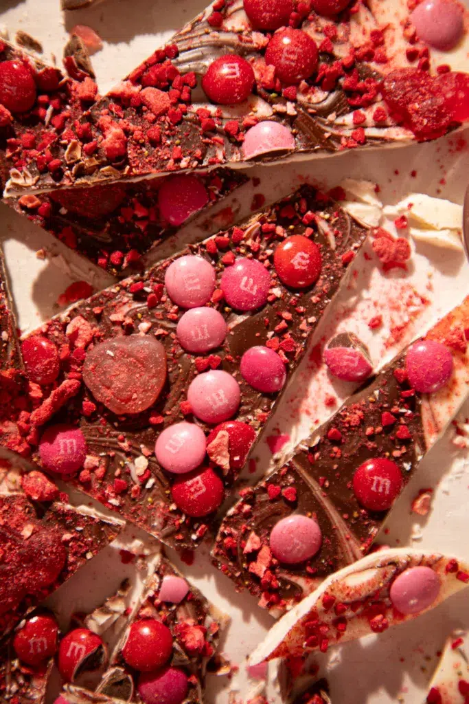 Overhead view of sliced no-bake Valentine’s Day gummy bark on parchment paper with heart gummies, M&Ms, and crushed strawberry pieces.