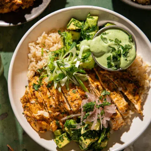 Yogurt marinated cilantro lime chicken served over rice with avocado, green onions, pickled onions, and creamy green sauce.