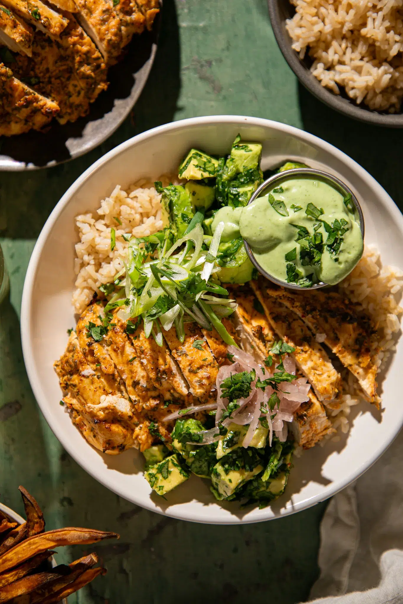 Yogurt marinated cilantro lime chicken served over rice with avocado, green onions, pickled onions, and creamy green sauce.