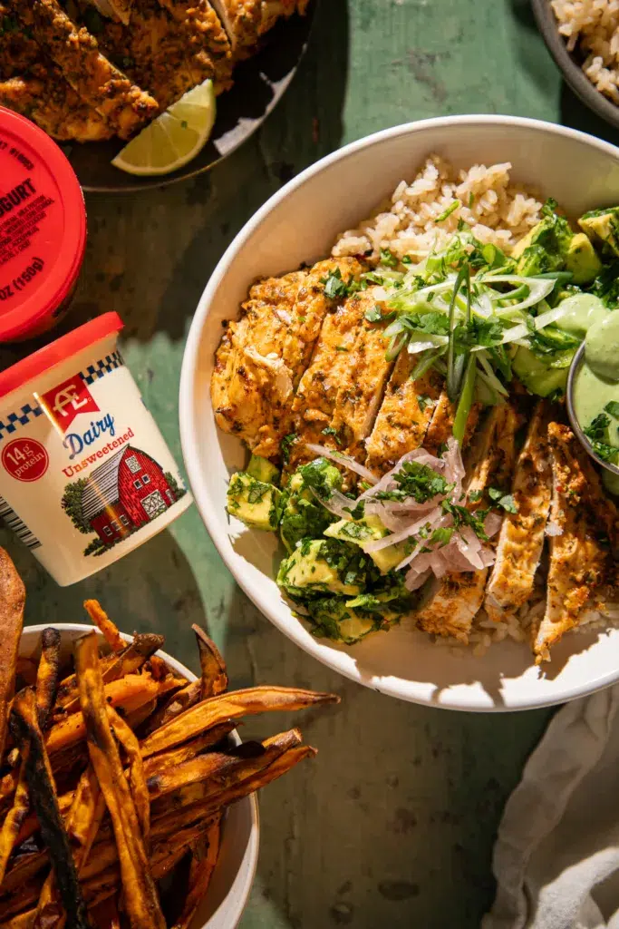 Yogurt marinated cilantro lime chicken served over rice with avocado, green onions, pickled onions, and creamy green sauce.