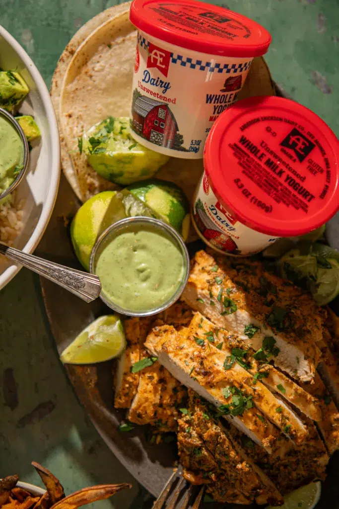 Sliced cilantro lime chicken with fresh herbs served alongside creamy yogurt sauce and whole milk yogurt containers.