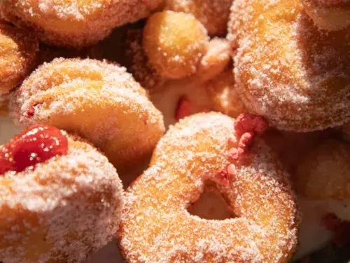 Close-up of strawberry sugar biscuit donuts showing golden edges, pink sugar coating, and strawberry jelly centers.