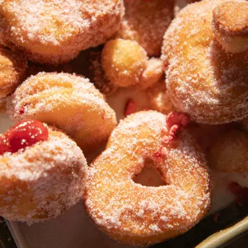 Close-up of strawberry sugar biscuit donuts showing golden edges, pink sugar coating, and strawberry jelly centers.