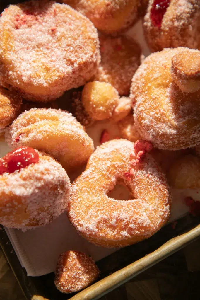 Close-up of strawberry sugar biscuit donuts showing golden edges, pink sugar coating, and strawberry jelly centers.