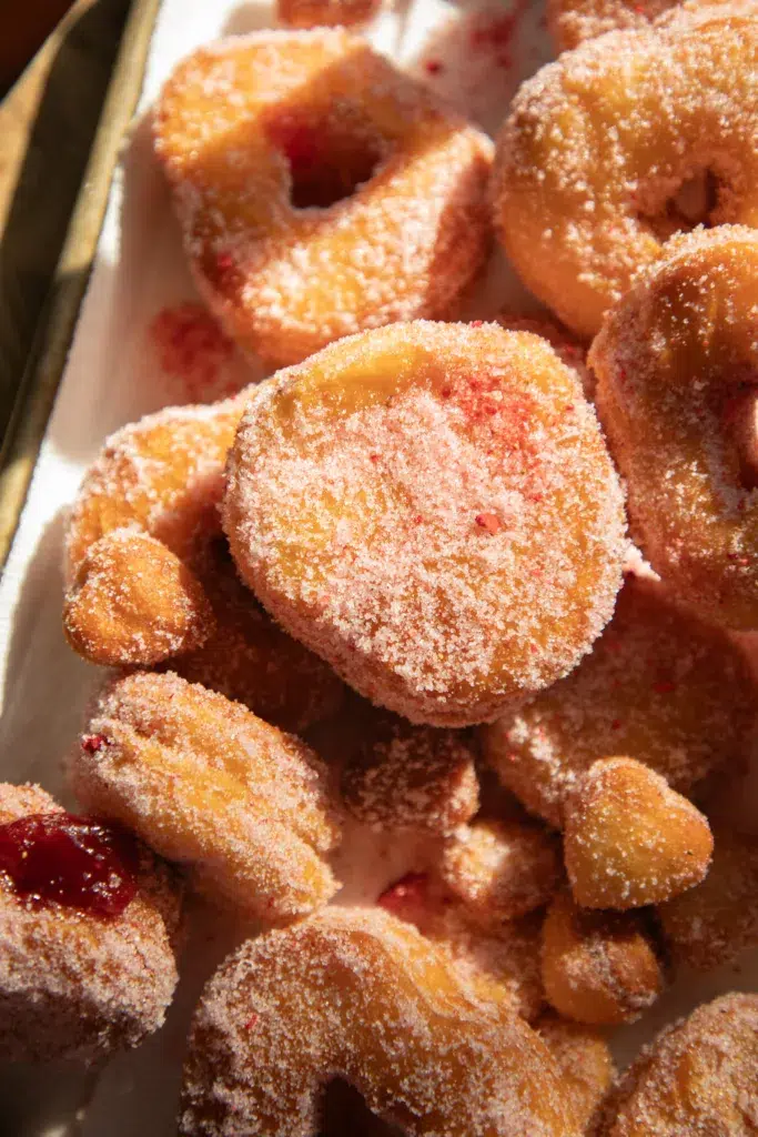Tray of heart-shaped biscuit donuts coated in strawberry sugar with visible strawberry jelly filling.