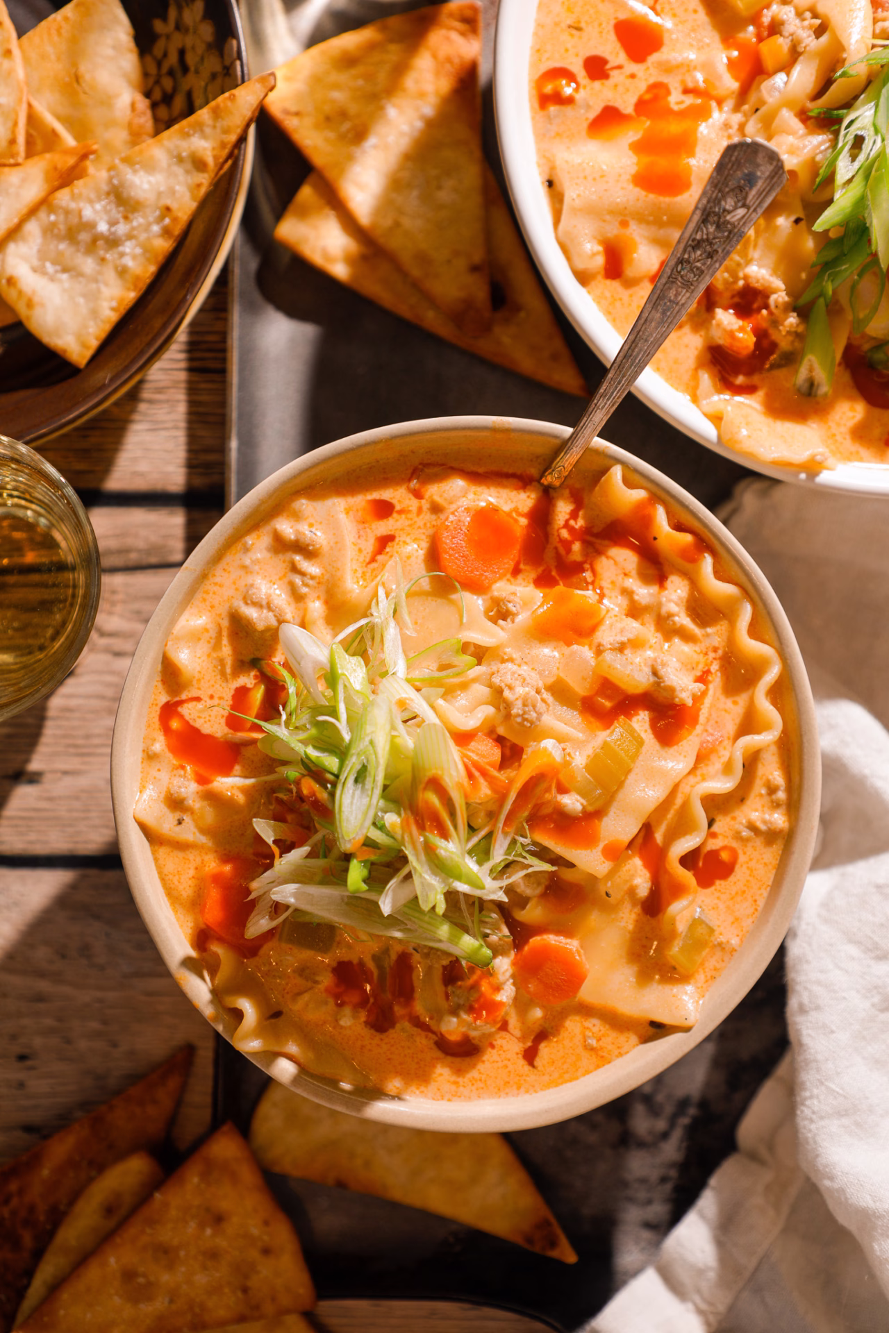 Two bowls of buffalo chicken lasagna soup with lasagna noodles, ground chicken, carrots, celery, and hot sauce drizzle, served alongside crispy tortilla chips.