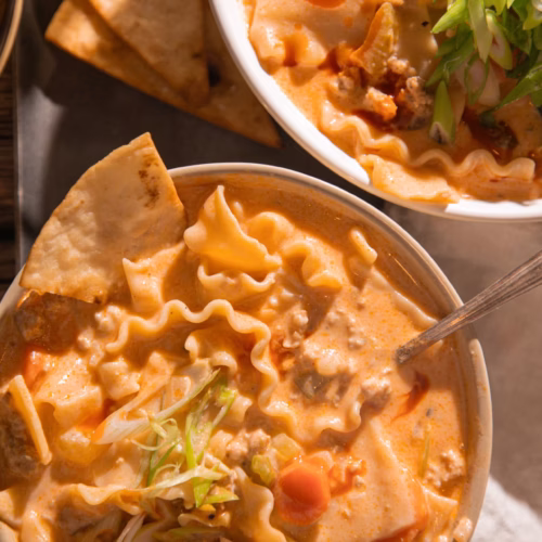 Close up of creamy buffalo chicken lasagna soup showing tender lasagna noodles, ground chicken, vegetables, and rich orange broth.