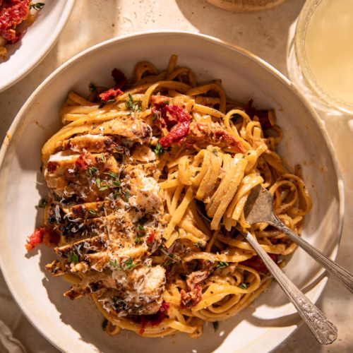 Close-up of creamy Tuscan chicken pasta with linguine, sun-dried tomatoes, parmesan, and sliced chicken breast.