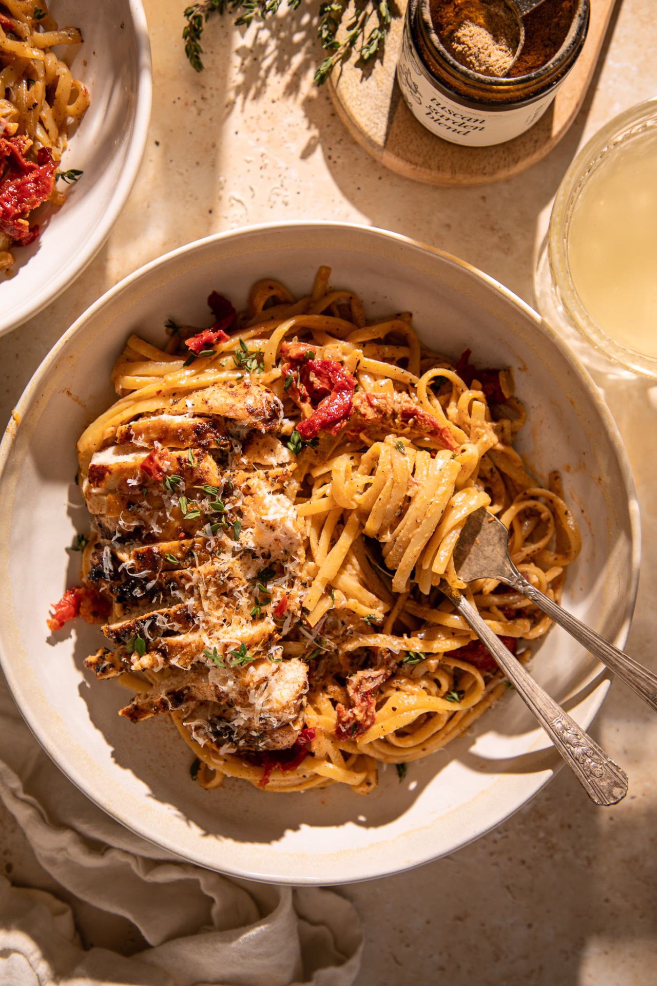 Close-up of creamy Tuscan chicken pasta with linguine, sun-dried tomatoes, parmesan, and sliced chicken breast.