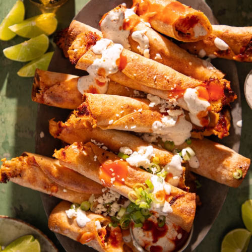 Crispy Nashville hot chicken taquitos topped with sauce, cheese, and green onions