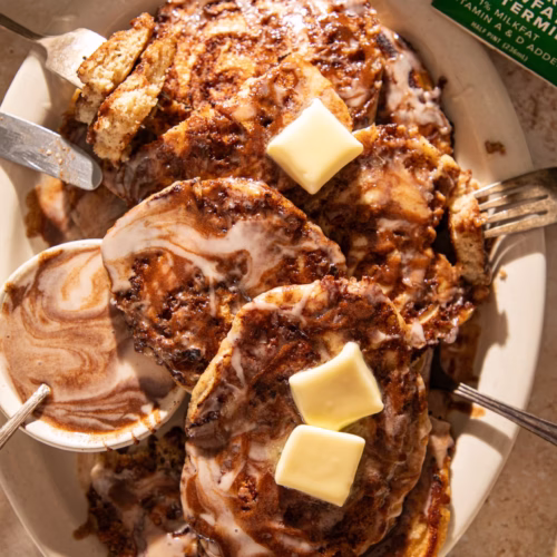 Cinnamon roll pancakes served with glaze and a side of syrup showing the cinnamon swirl detail