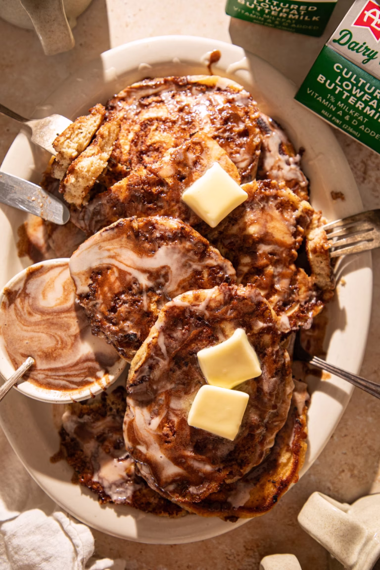 Cinnamon roll pancakes served with glaze and a side of syrup showing the cinnamon swirl detail