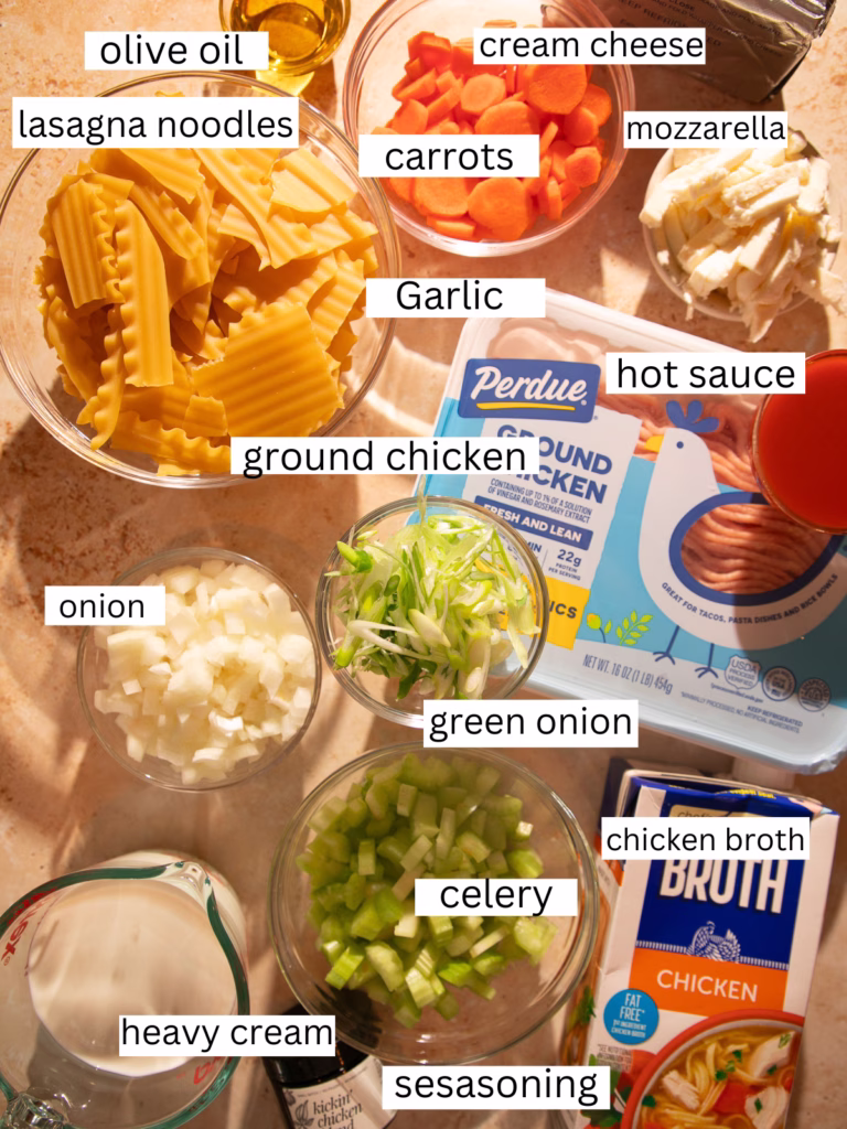 Ingredients for buffalo chicken lasagna soup including ground chicken, lasagna noodles, cream cheese, mozzarella, carrots, celery, onion, garlic, heavy cream, chicken broth, hot sauce, olive oil, green onions, and Kickin’ Chicken seasoning.